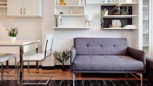 A modern living room with a grey sofa, a small table, a chair, and a potted plant. - Xin Hotel at Udomsuk 25 (Bangkok)