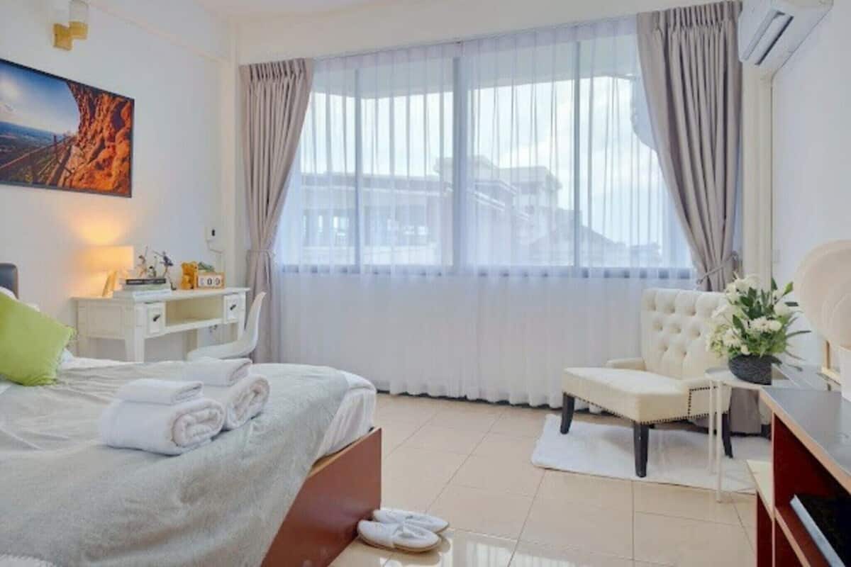A hotel room with a bed, a desk, a chair, and a large window with curtains.