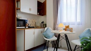 A compact kitchen with white cabinets, a microwave, and a small dining table with two chairs. - Xin Hotel at Udomsuk 25 (Bangkok)