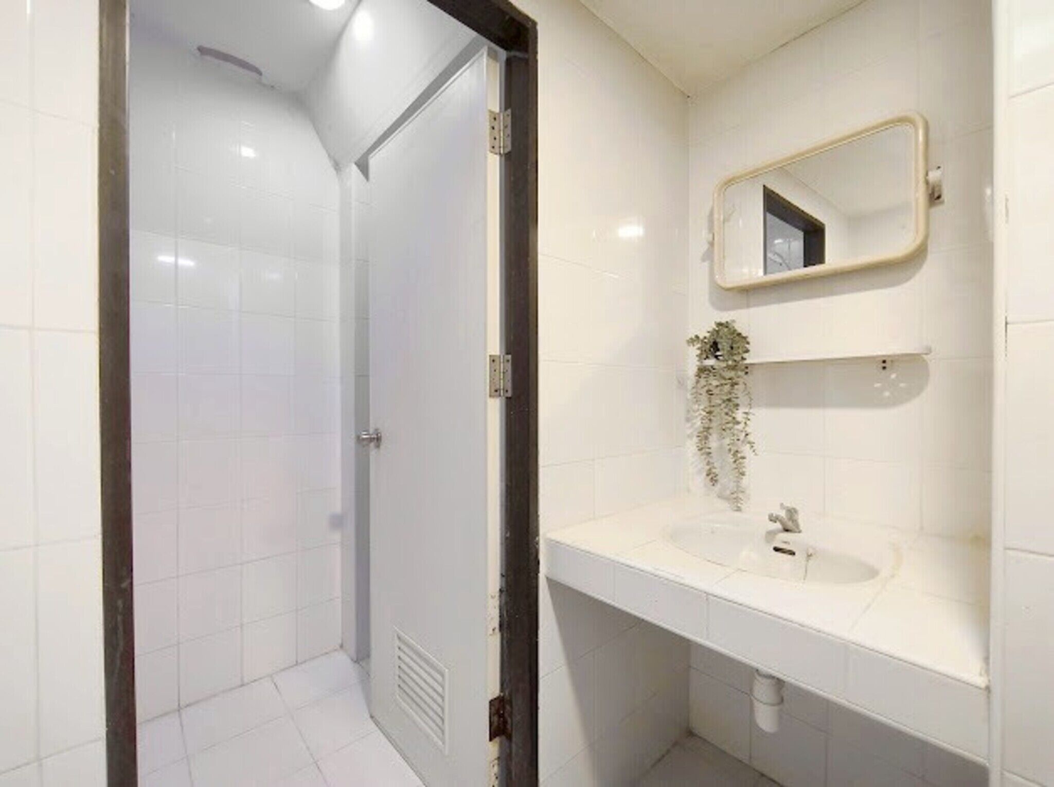 Een badkamer met een wit wastafel, spiegel en een deur naar de douche.