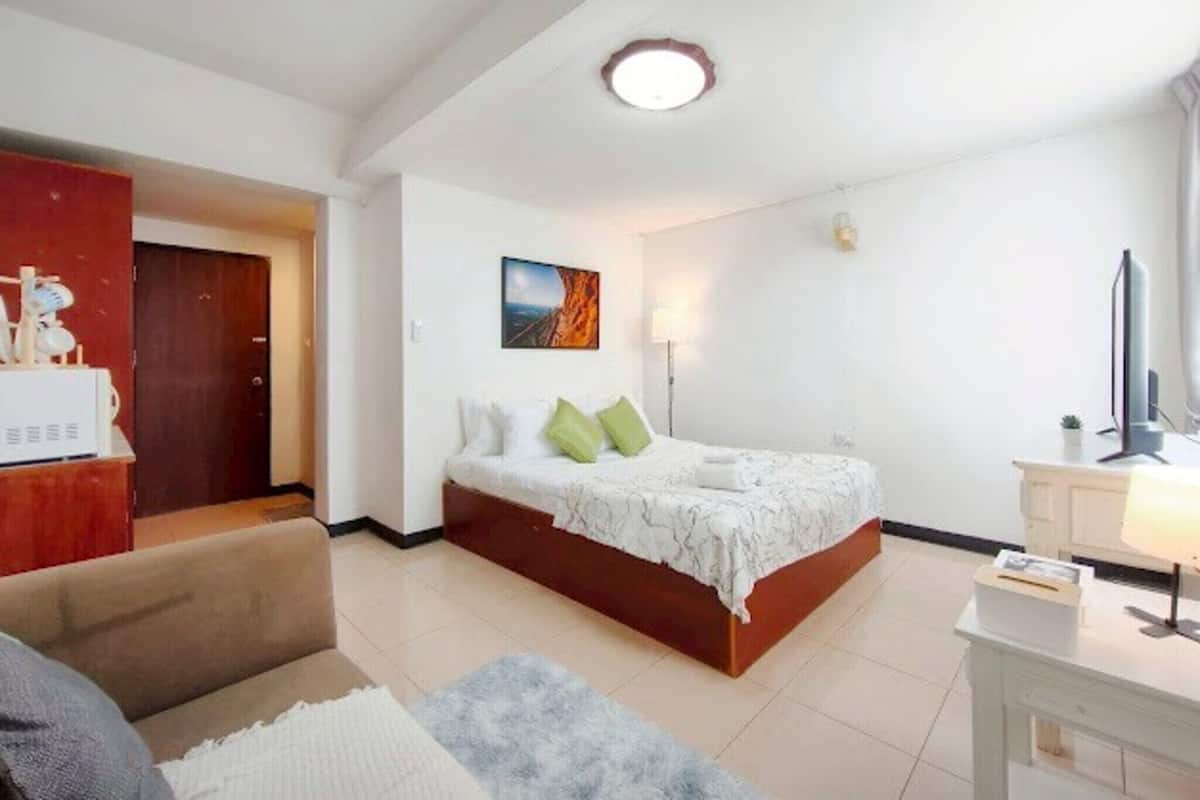 A bedroom with a bed, a desk, a television, and a painting on the wall.
