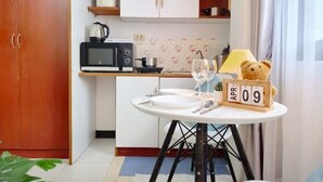 A compact kitchen with a microwave, kettle, and shelves above the counter. There's a small dining table with a clock displaying 'APR 09'. - Xin Hotel at Udomsuk 25 (Bangkok)