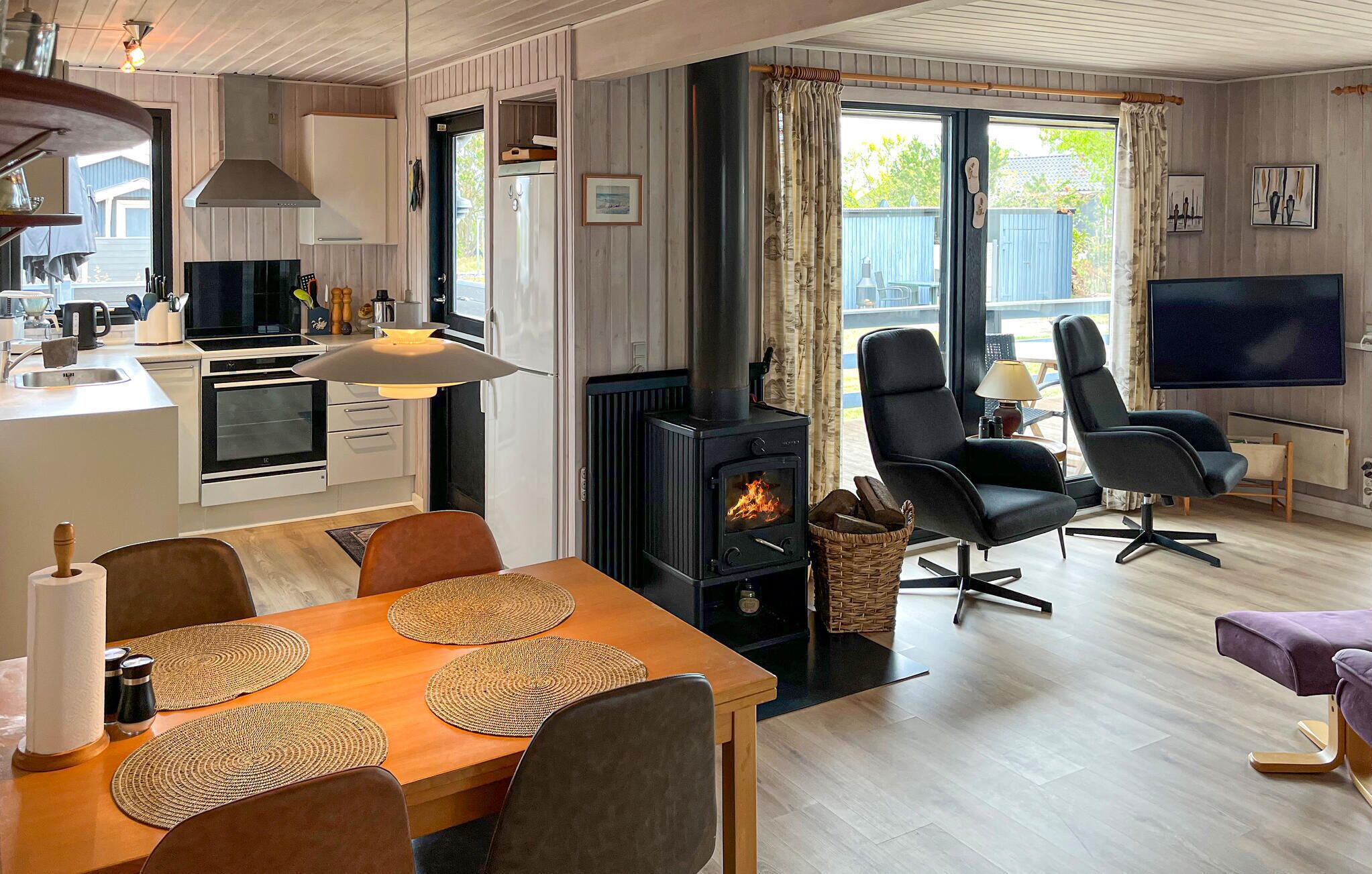 A modern kitchen with a stove, dining table with placemats, and a TV in a living area with chairs.
