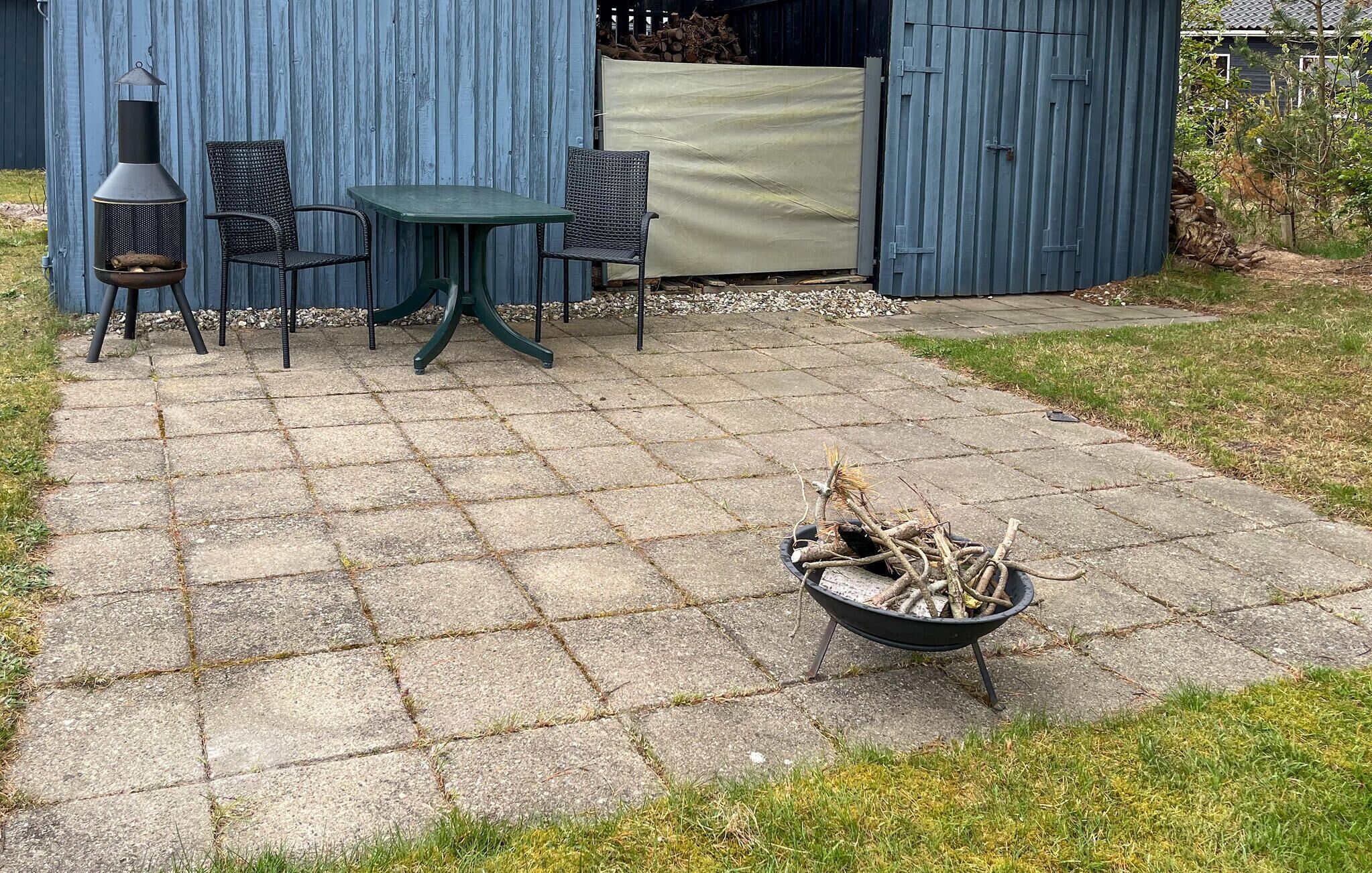 Eine Terrasse mit Steinplatten, einem Metallgrill, zwei Korbstühlen und einem Tisch.