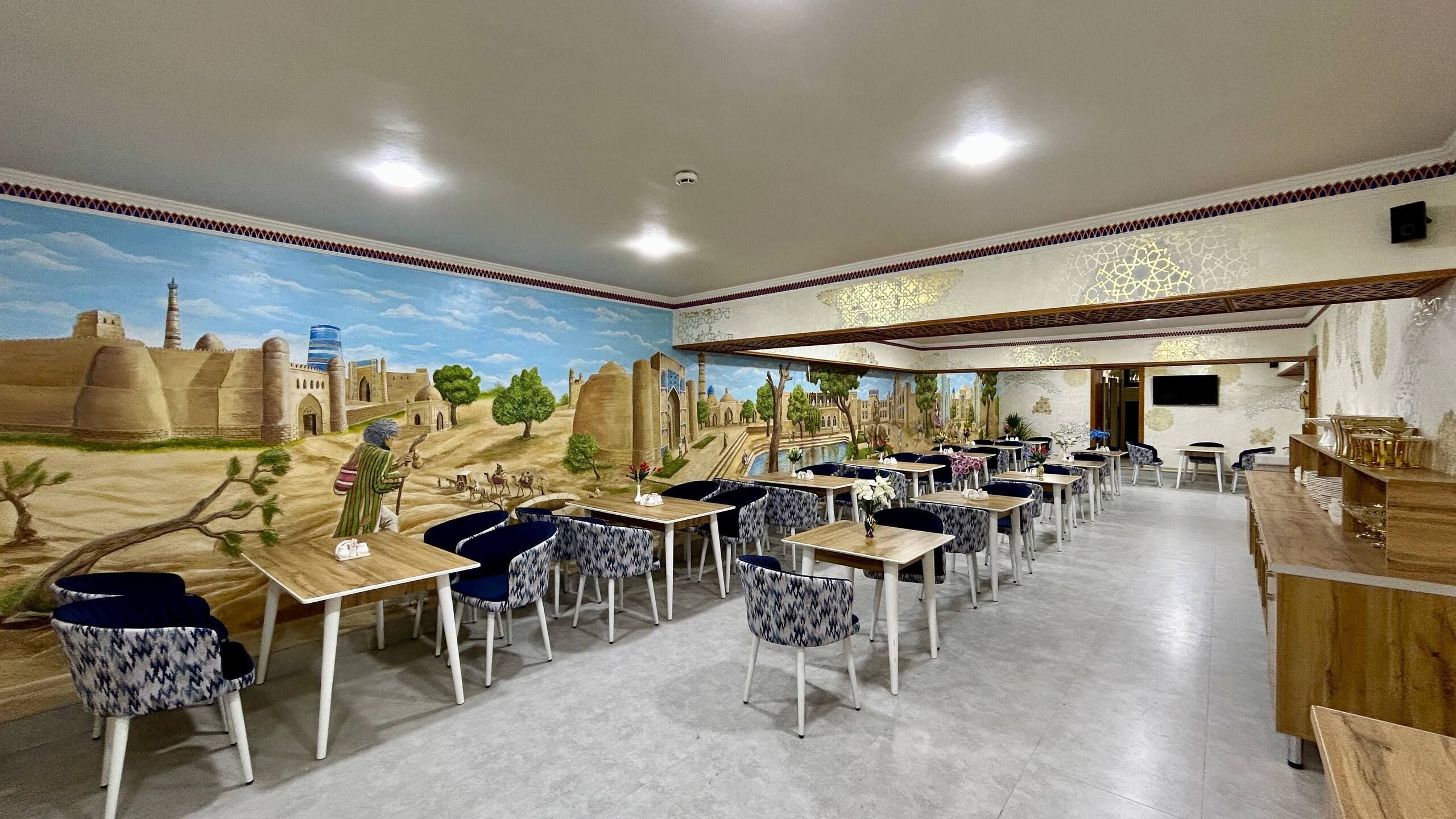 A restaurant with a desert-themed mural, multiple tables, and chairs.