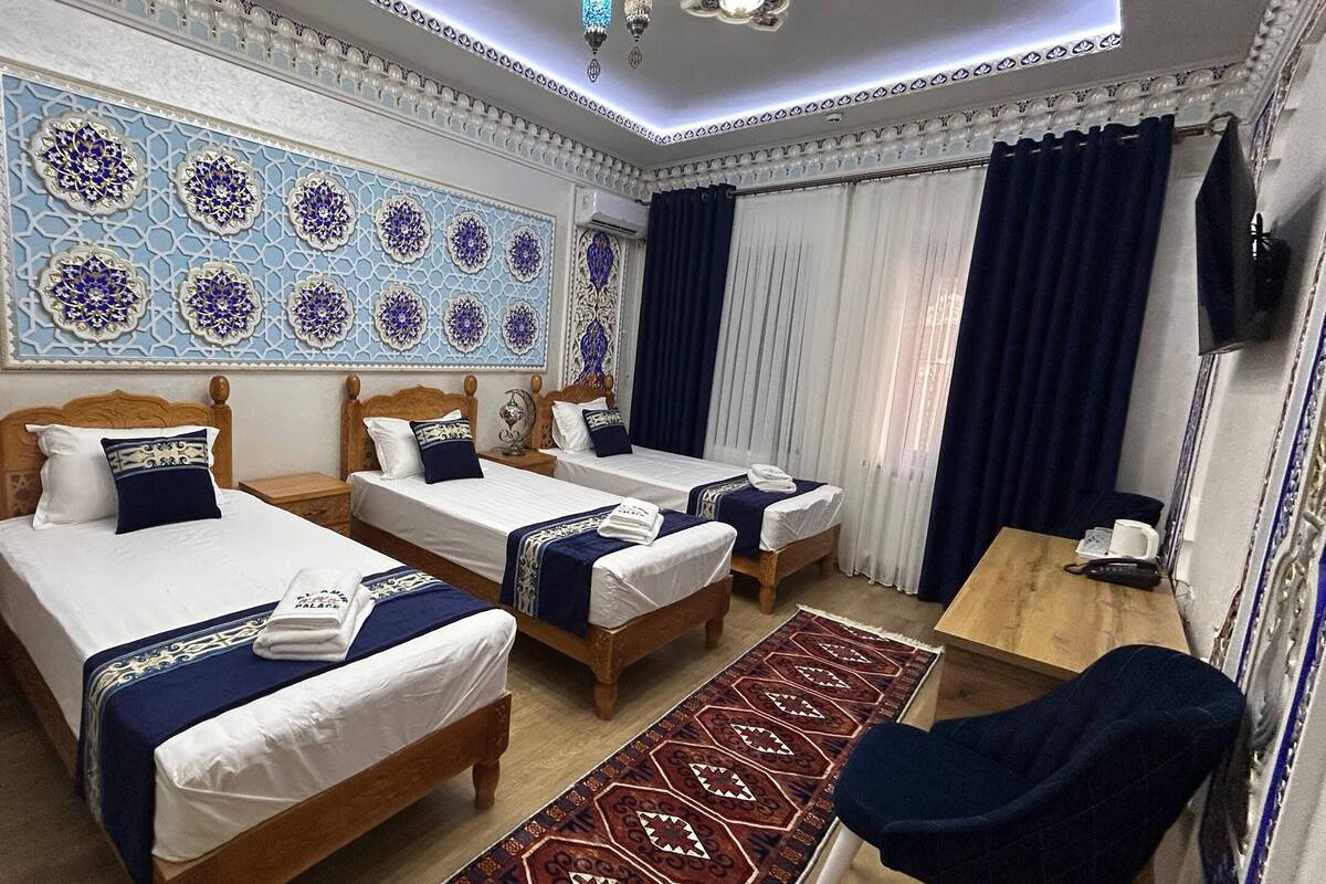 Quarto de hotel com três camas de madeira, uma escrivaninha de madeira, um tapete estampado e um grande painel decorativo na parede.