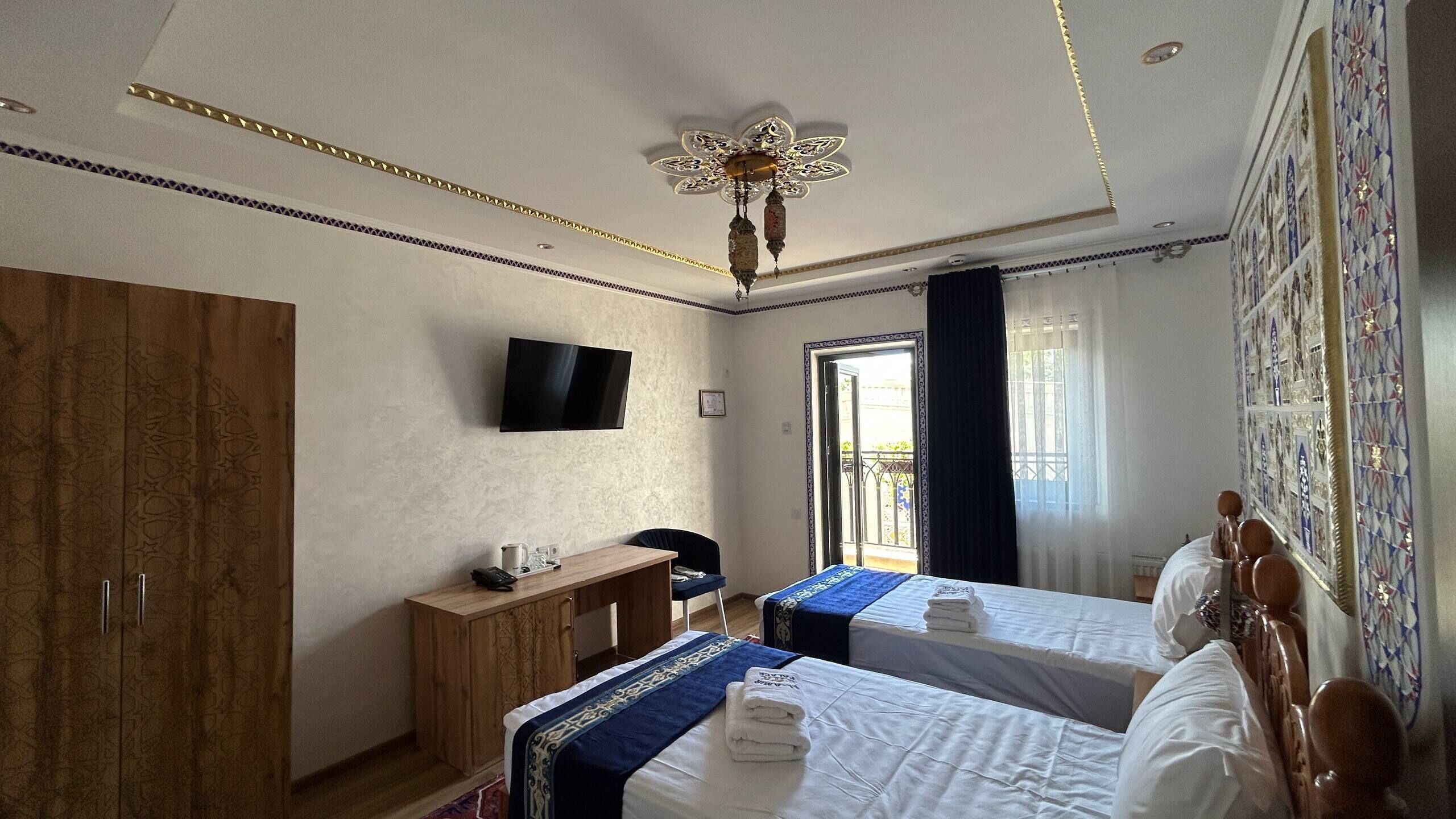 A hotel room with two beds, a desk, a television, and a ceiling fan.