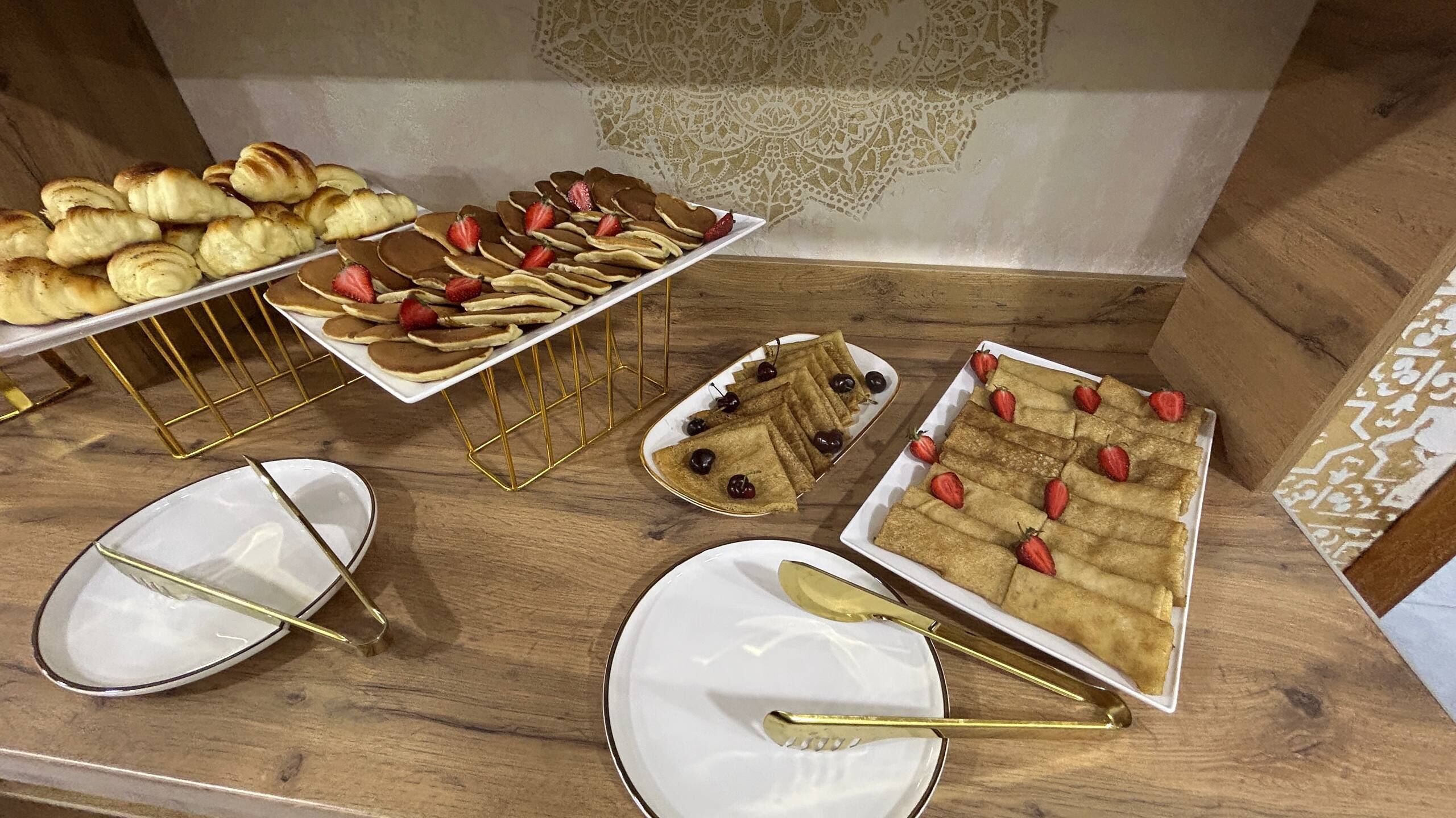 A buffet table with various food items, including pancakes, croissants, and crepes, arranged on white plates with gold handles.