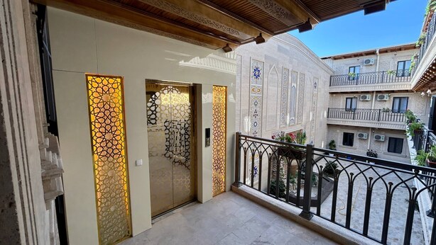 A balcony with a wrought iron railing, a door with decorative glass panels, and a view of a building with patterned windows and balconies.