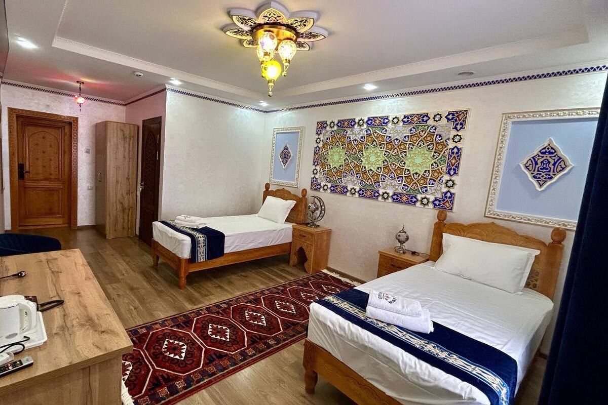 Quarto de hotel com duas camas, uma escrivaninha de madeira, cafeteira, comando de televisor e tapete estampado.