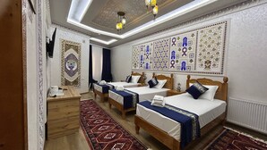 A hotel room with three beds, a wooden desk, a patterned rug, and decorative wall art.