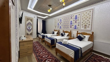 Una habitación de hotel con tres camas, un escritorio de madera, un tapete estampado y decoración en la pared.