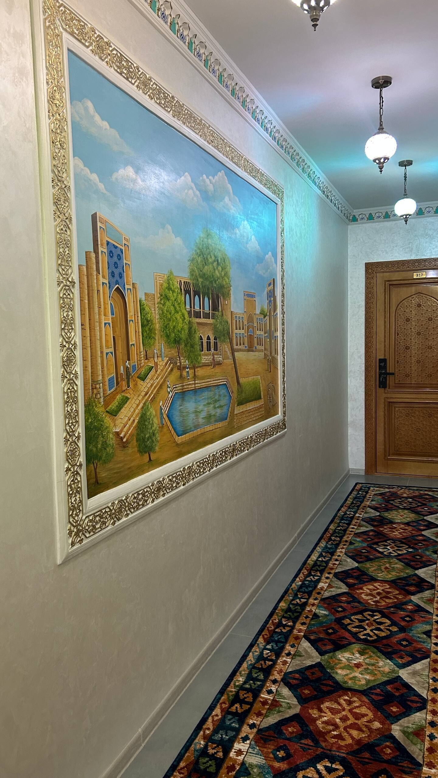 Un pasillo con un gran mural, una alfombra estampada y una puerta de madera.