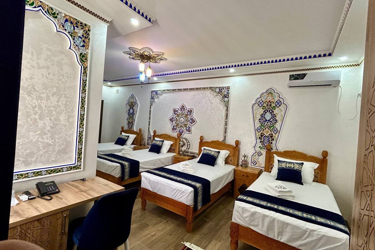 Quarto de hotel com três camas, uma escrivaninha com telefone e painéis decorativos na parede.