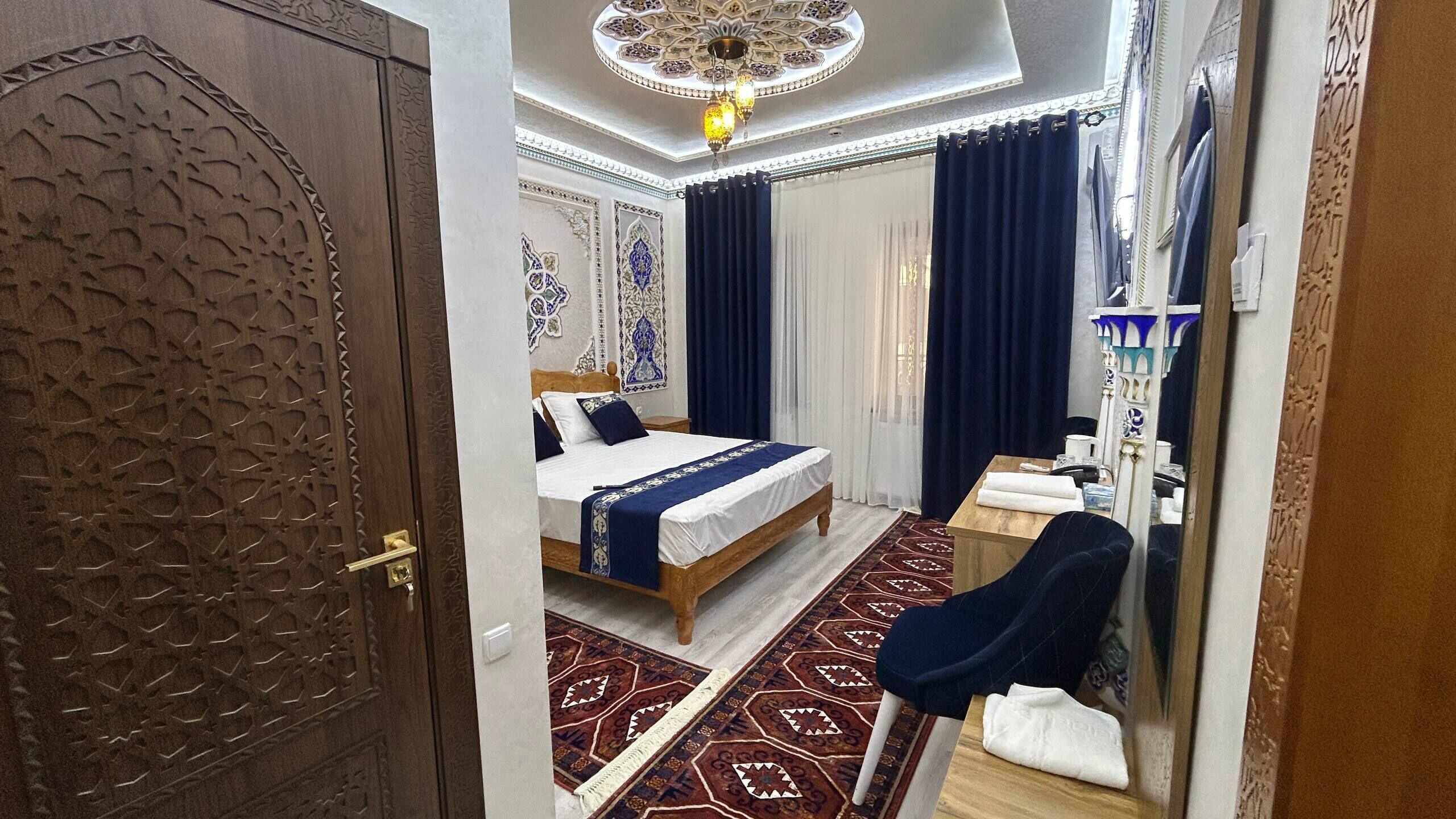 A room with a bed, a desk, a chair, a mirror, and a patterned rug.