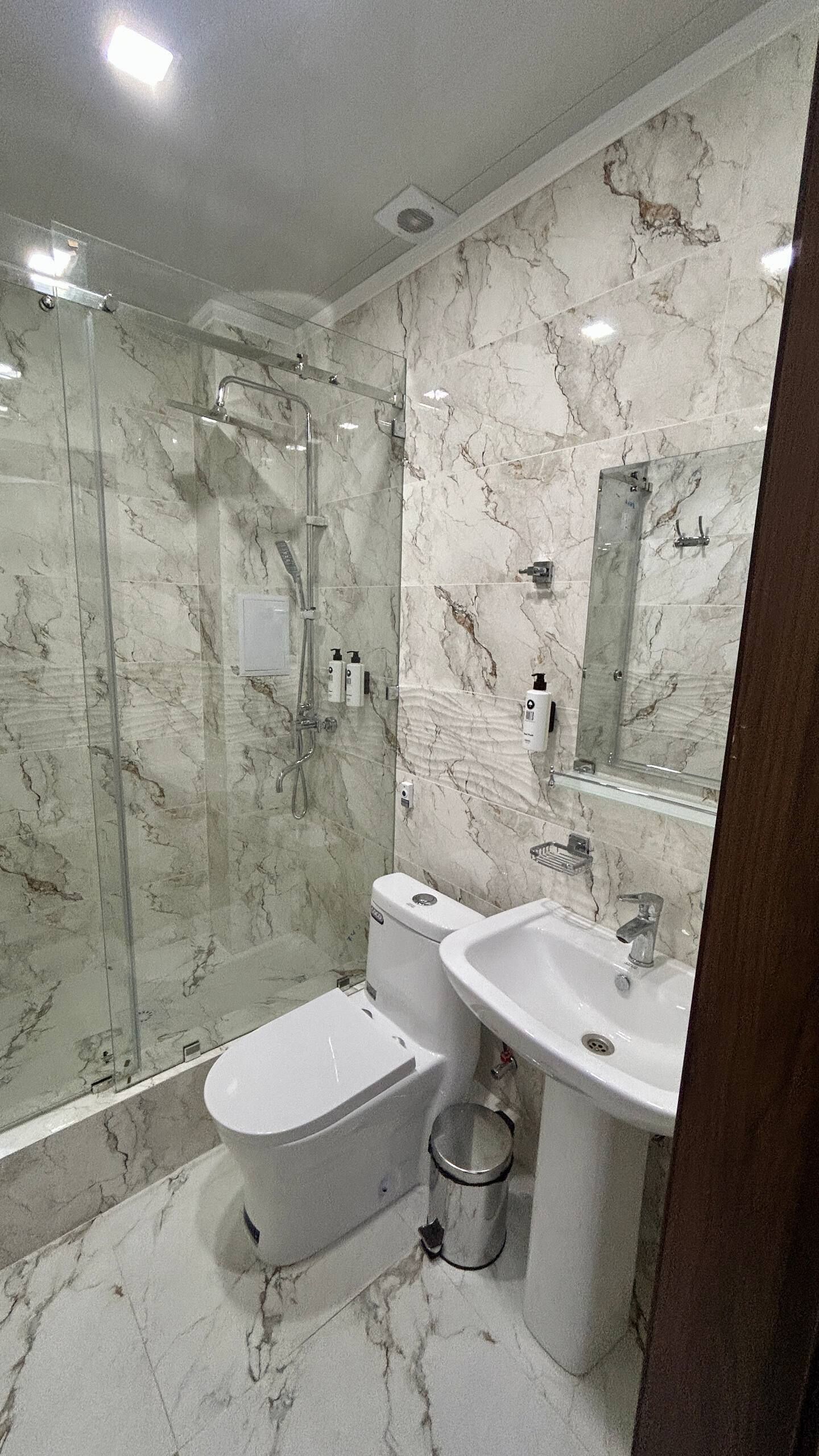 A modern bathroom with a glass-enclosed shower, a toilet, and a sink.