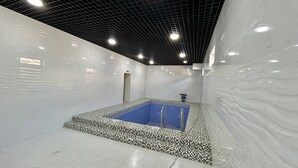 A large indoor swimming pool with a checkered tile border, surrounded by white walls and a black ceiling grid.