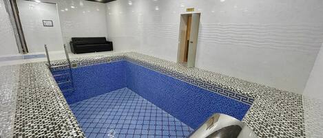 A swimming pool with mosaic tiles, a black bench, and a door.