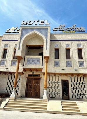 Ein Gebäude mit einem Schild, auf dem 'HOTEL' und 'Al-Amir Palace' über dem Eingang stehen, das einen traditionellen Baustil mit rundbogigen Durchgängen und verzierten Fenstern aufweist.