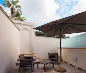 Eine Terrasse mit Tisch und Stühlen, einem großen Sonnenschirm und einer Treppe, die zu einer erhöhten Ebene führt.