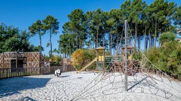 A sandy beach with playground equipment, a wooden structure, and a tall tree.