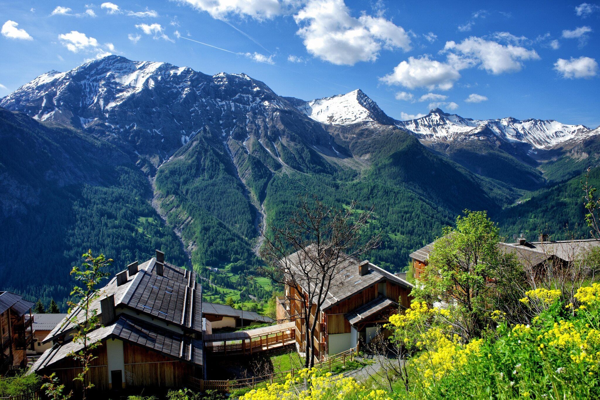 Un pueblo de montaña con casas de madera tradicionales, cielo despejado y picos nevados al fondo.