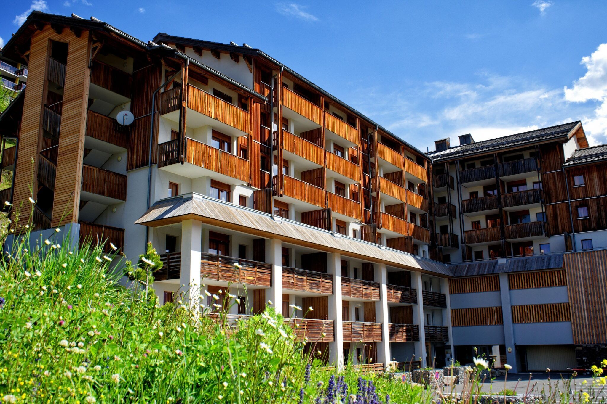 Un hotel de varios pisos con balcones de madera, un vestíbulo cubierto y un patio con vegetación.