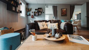 Un salon moderne avec un canapé en cuir, des étagères, une table basse agrémentée d’objets décoratifs et, au fond, un coin repas.