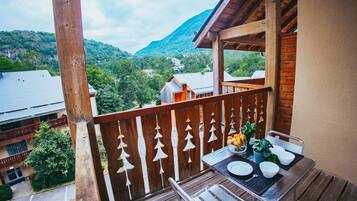 A balcony with a wooden railing, a table with chairs, and a view of a mountainous landscape.