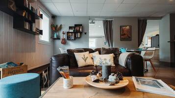 A modern living room with a leather sofa, bookshelves, a coffee table with decorative items, and a dining area in the background.