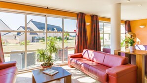 Ett modernt vardagsrum med en röd soffa, ett soffbord och utsikt över ett bostadsområde genom stora fönster.
