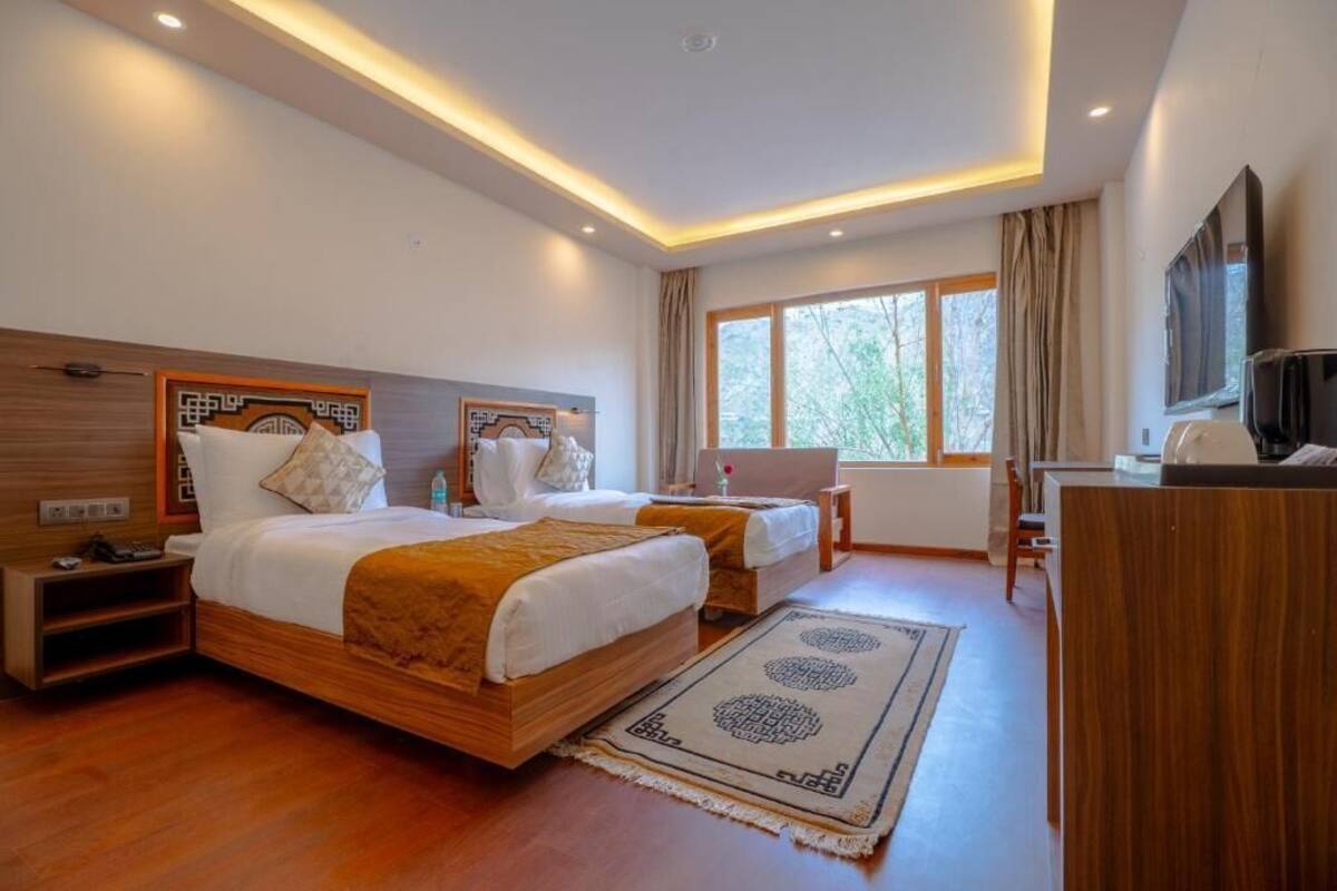 A hotel room with two beds, a desk, a TV, and a large window.