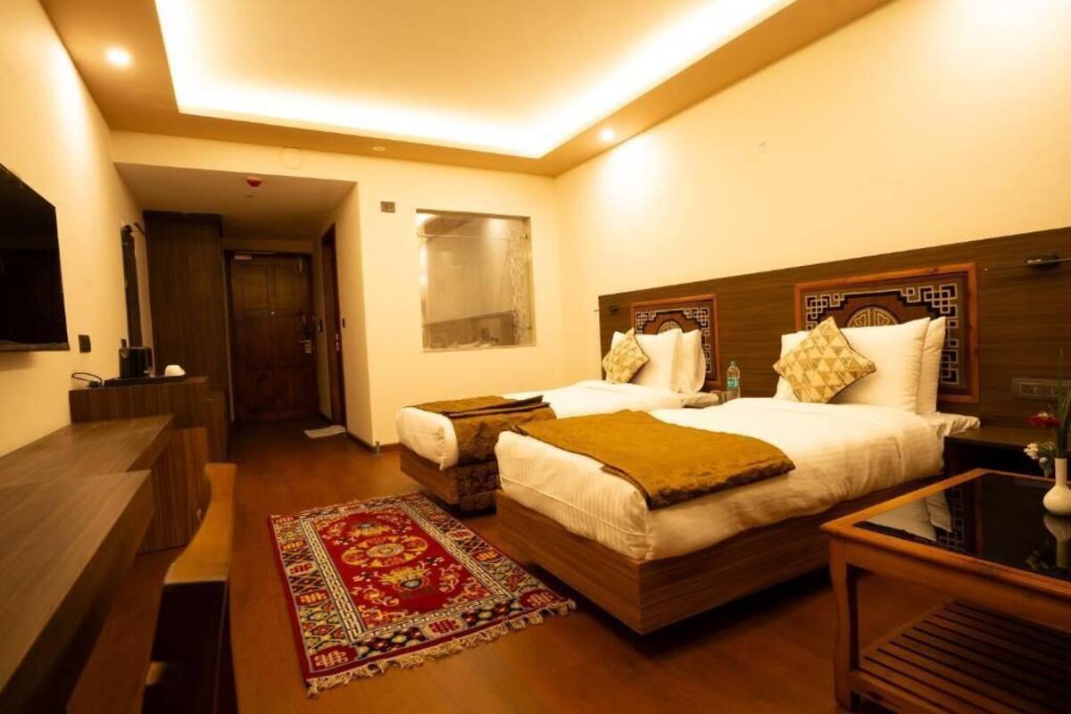 A hotel room with a bed, bedside tables, a desk, a mirror, a window, and a red patterned rug.