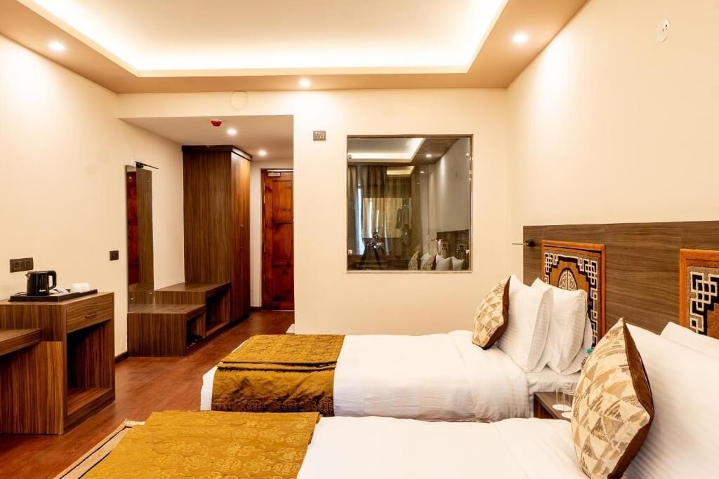Habitación de hotel con dos camas, un escritorio con cafetera, un espejo y cabecero de madera.