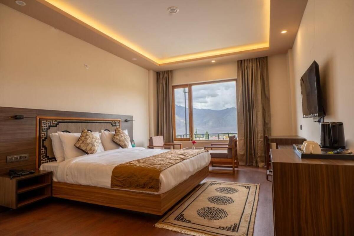 A hotel room with a large bed, a desk, a TV, and a view of mountains.