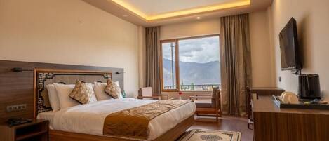 A hotel room with a large bed, a desk, a TV, and a view of mountains.