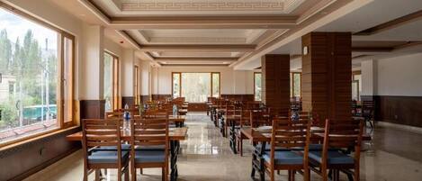 A spacious dining area with wooden tables and chairs, large windows, and a decorative ceiling.