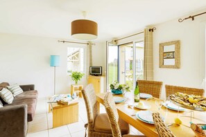 A dining area with wicker chairs, a wooden table, and a TV on a stand. - Breton Duplex Cottage Retreat (Cancale)