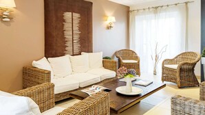 Ein Wohnzimmer mit einem weißen Sofa, Korbstühlen, einem Couchtisch und Wandleuchten.
