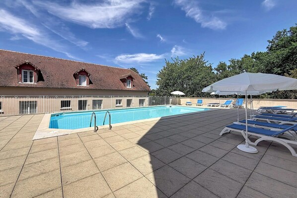 A swimming pool with lounge chairs and umbrellas, surrounded by a building with a tiled roof.