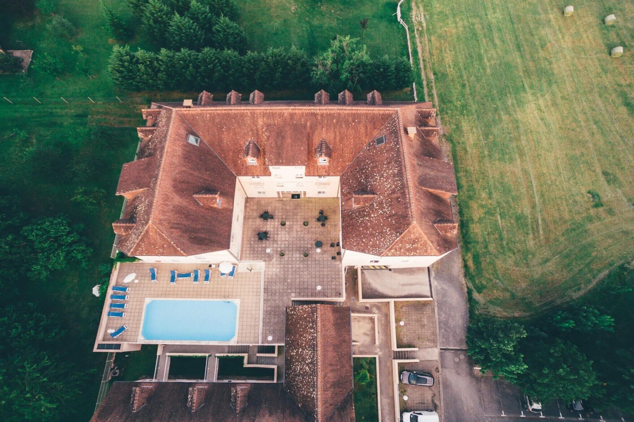 Luftaufnahme eines Gebäudes mit Innenhof, Schwimmbecken und Parkplatz.