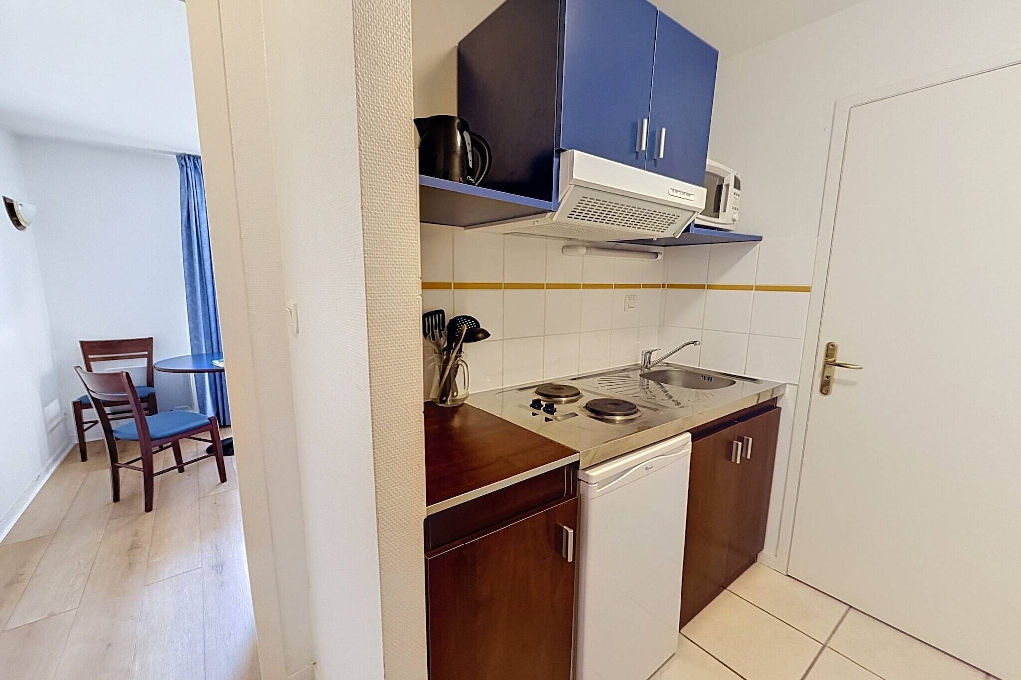 Cocina compacta con estufa, pileta y alacenas, y un comedor con una silla y mesa.