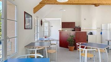 A kitchen with wooden beams, a dining area with tables and chairs, and a view through the window.