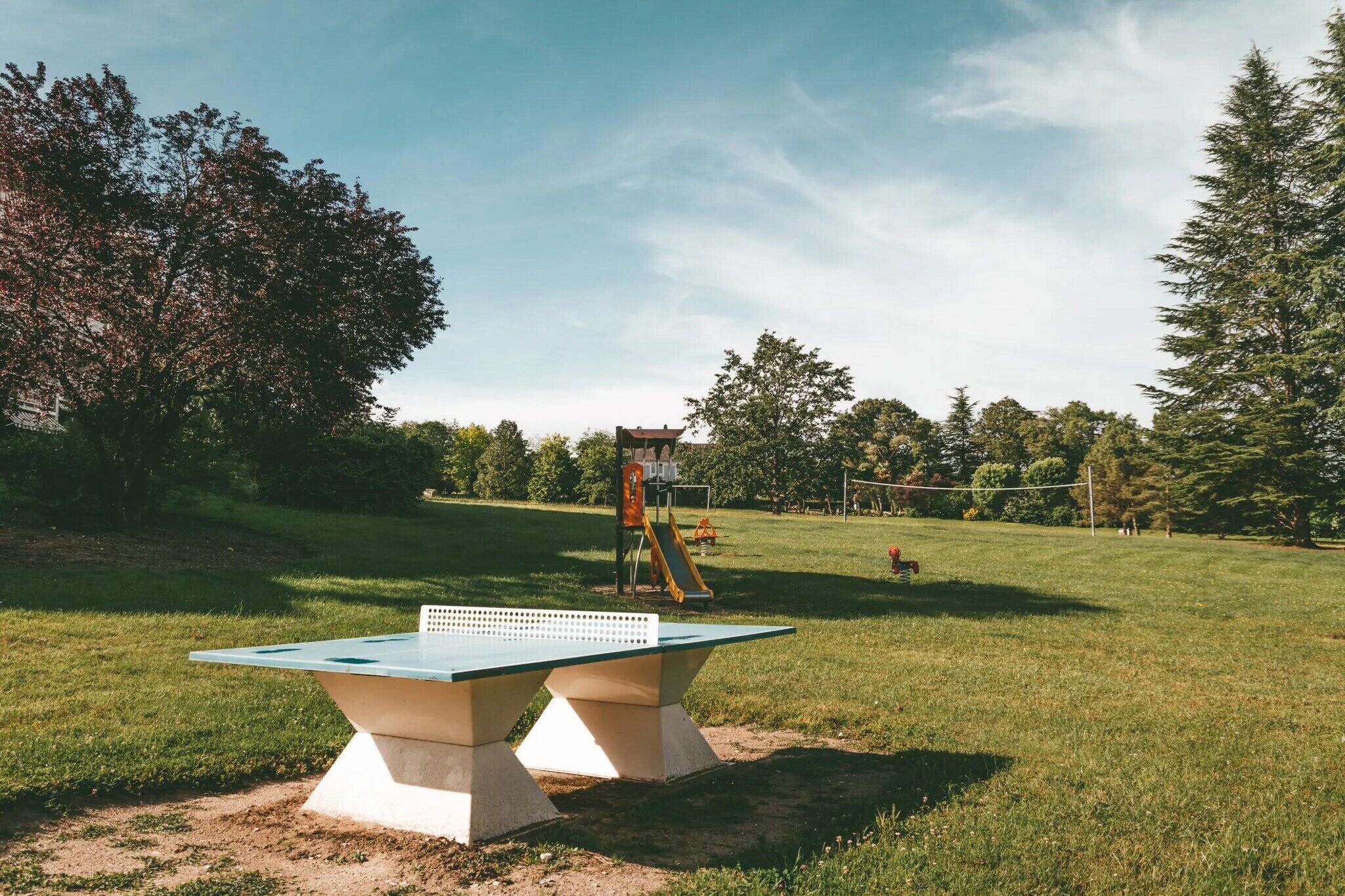 Una mesa de ping pong en un parque, con un área de juegos al fondo.
