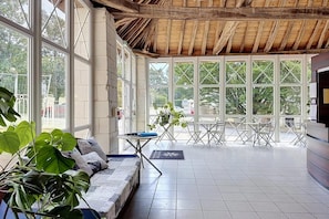 A spacious room with large windows, a wooden ceiling, and a seating area with a sofa and tables. - Cozy Couples Stay Near Thermal Spa (La Roche-Posay)