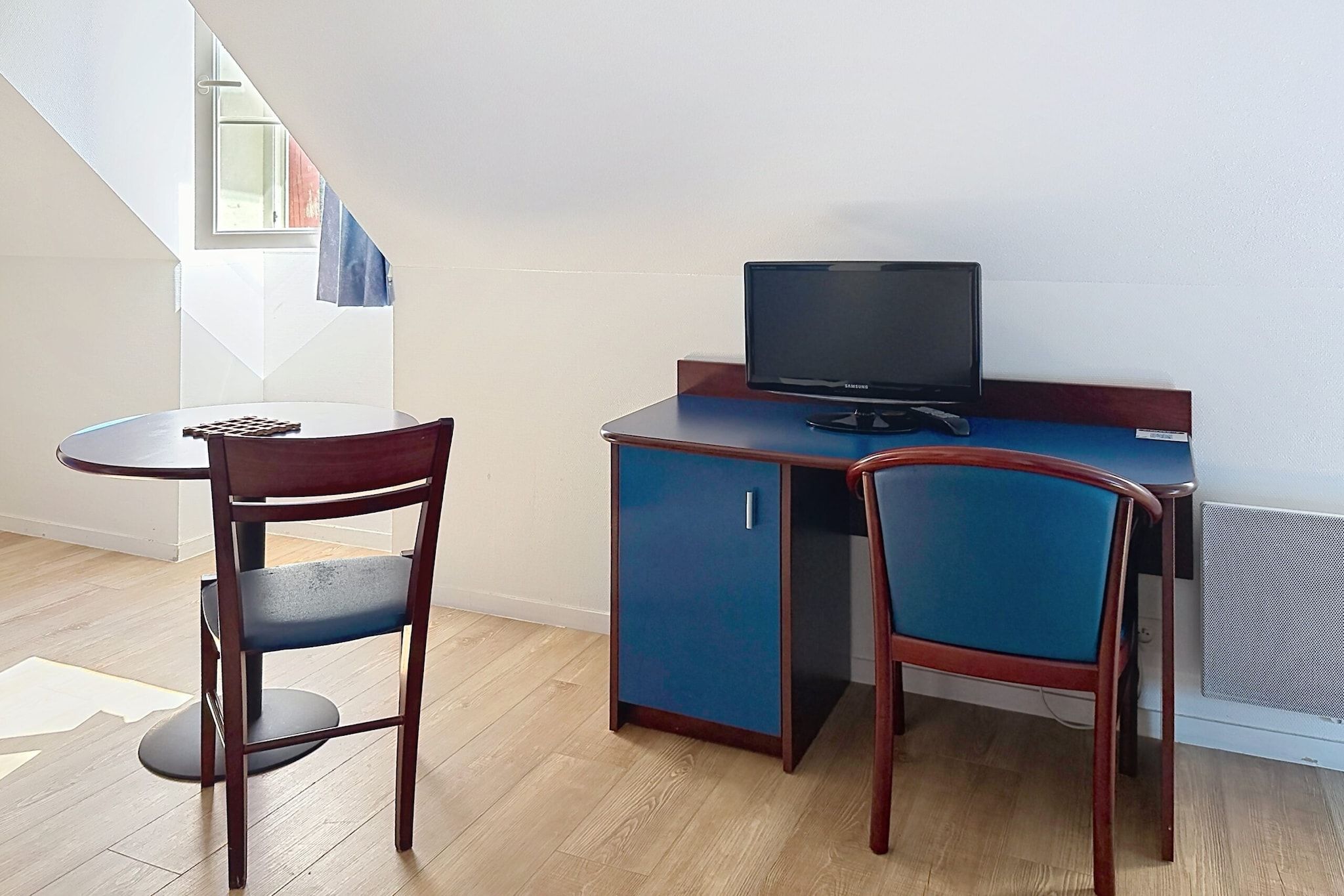 A small room with a desk, two chairs, a television, and a window.