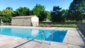 En swimmingpool med en bygning af sten og liggestole i baggrunden.
