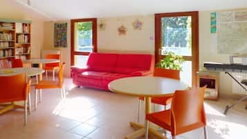 Ein Zimmer mit einem roten Sofa, orangenen Sesseln, einem runden Tisch, einem Bücherregal und einer Tastatur.