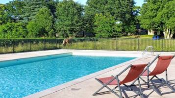 A swimming pool with a metal fence, two lounge chairs, and trees in the background.