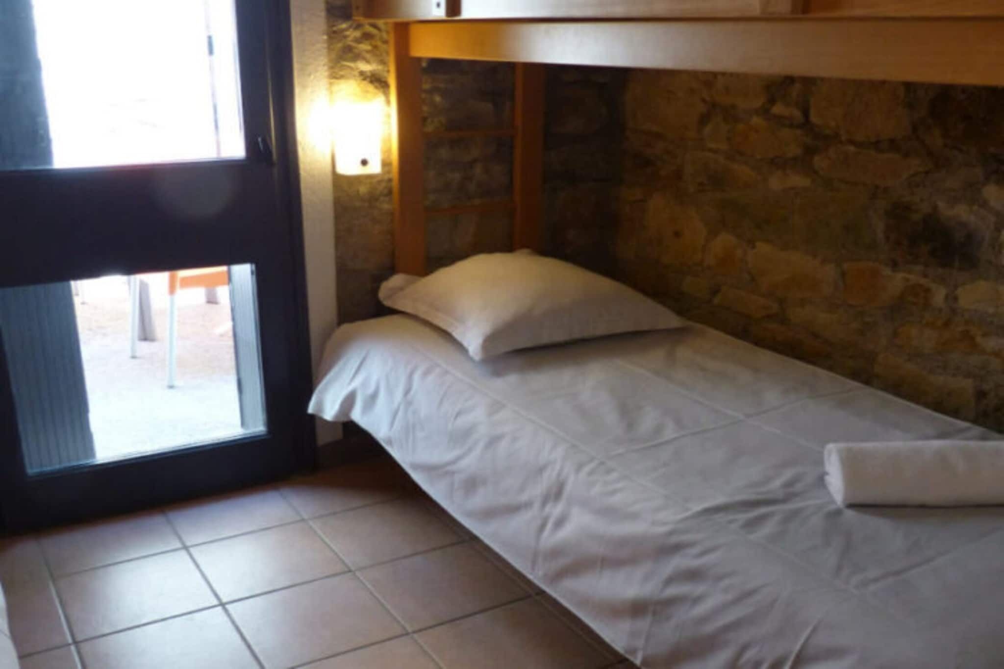 Ein Einzelbett mit weißer Matratze und Kissen, eine Steinwand und ein Fenster mit Blick ins Freie.